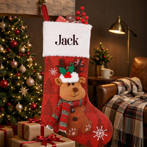 Personalized red Christmas stocking with a plush reindeer hanging beside a decorated fir tree at night