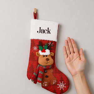 Personalized red stocking with a plush reindeer beside an open adult palm on a plain wall, showing its scale