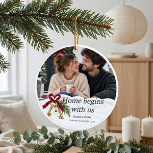 Personalized first home Christmas ornament hanging from a pine branch in a bright room, white candles and a paper lantern beside it