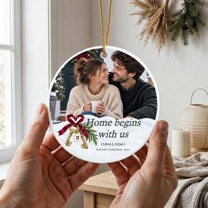 Two hands holding the personalized first home Christmas ornament up by its gold cord in a bright room