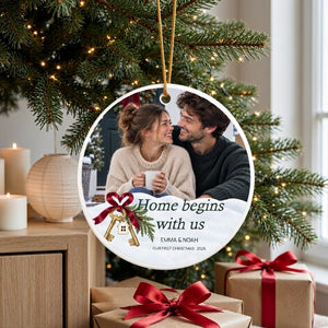 Personalized first home Christmas ornament hanging on a decorated tree with kraft gifts tied with red ribbon at the base
