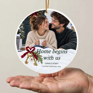 Personalized first home Christmas ornament held above an open adult palm, showing its 5 in scale against a plain wall